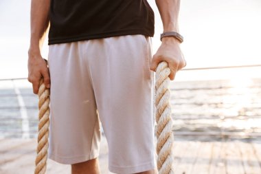Deniz kenarındaki ahşap iskelede fitness ipi tutan eşofmanlı kafkas adamın fotoğrafı kırpıldı