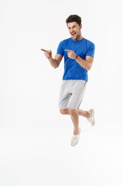 Yakışıklı mutlu genç spor fitness adam beyaz duvar arka plan üzerinde izole ayakta parmakları jest ile işaret yapmak.