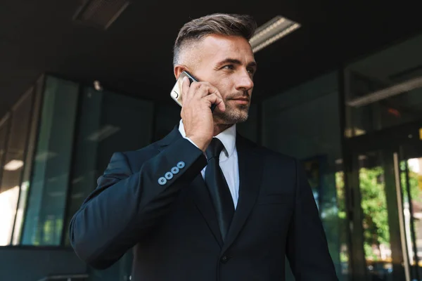 Концентрований зрілий сіроокий красивий бізнесмен на вулиці біля ділового центру розмовляє по мобільному телефону . — стокове фото