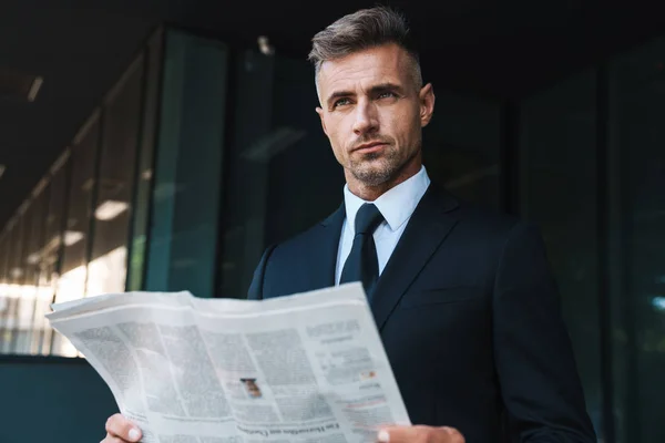 Súlyos érett csinos szürke hajú üzletember a szabadban, az utcán közelében Business Center olvasatban újság. — Stock Fotó