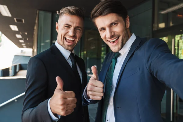 Фото радостных двух бизнесменов, показывающих большие пальцы вверх и принимающих SAL — стоковое фото
