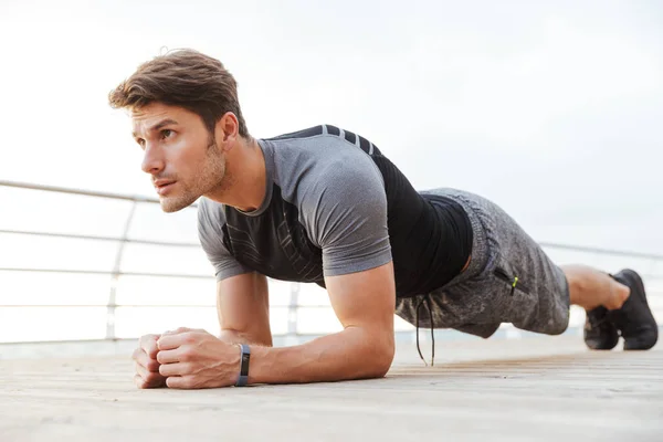 Foto eines männlichen Mannes im Trainingsanzug beim Planken auf einem hölzernen Pier am Meer — Stockfoto