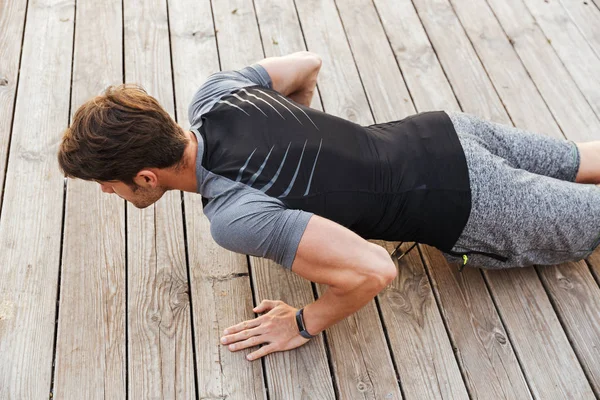 Foto de la parte superior del hombre masculino en chándal haciendo ejercicio mientras hace ejercicio en el muelle de madera en la playa — Foto de Stock