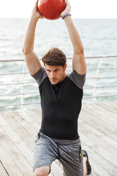 Fuerte serio concentrado joven deportista al aire libre hacer ejercicios con pelota . — Foto de Stock