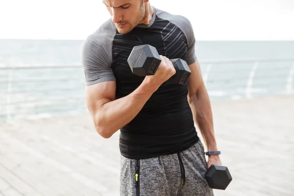 Grave concentrato giovane uomo sportivo all'aperto in spiaggia fare esercizi per la parte superiore delle braccia con manubri . — Foto Stock