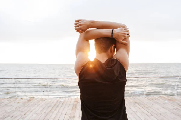 Foto de volta do jovem em traje de treino fazendo exercício enquanto trabalhava no cais de madeira à beira-mar — Fotografia de Stock