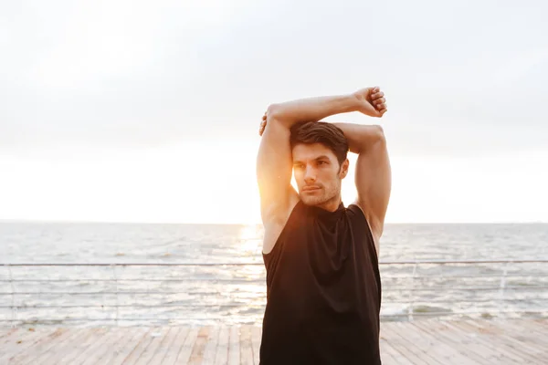 Foto guapo hombre en chándal haciendo ejercicio mientras hace ejercicio en el muelle de madera en la playa — Foto de Stock