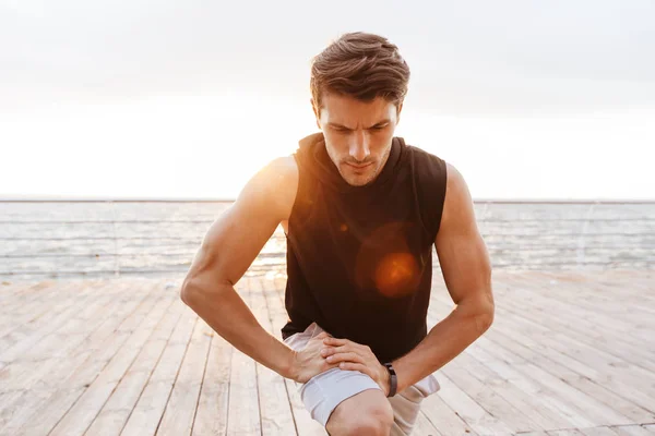 Foto do homem masculino em traje de treino fazendo exercício enquanto trabalhava no cais de madeira à beira-mar — Fotografia de Stock