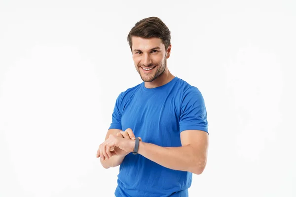 Счастливый молодой спортивный спортсмен, стоящий на белом фоне, используя часы . — стоковое фото