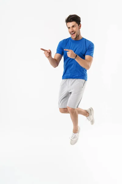 Beau jeune homme de fitness sportif heureux debout isolé sur fond de mur blanc faire pointer du doigt geste . — Photo