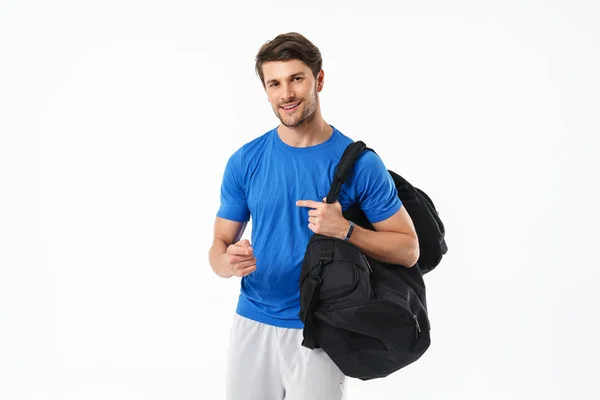 Joyeux optimiste beau jeune homme de fitness sportif debout isolé sur fond blanc mur tenant sac pointant vers vous . — Photo