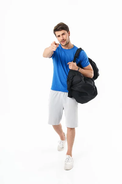Ernstige knappe jonge sport fitness man staande geïsoleerd over witte muur achtergrond Holding tas wijzend naar u. — Stockfoto