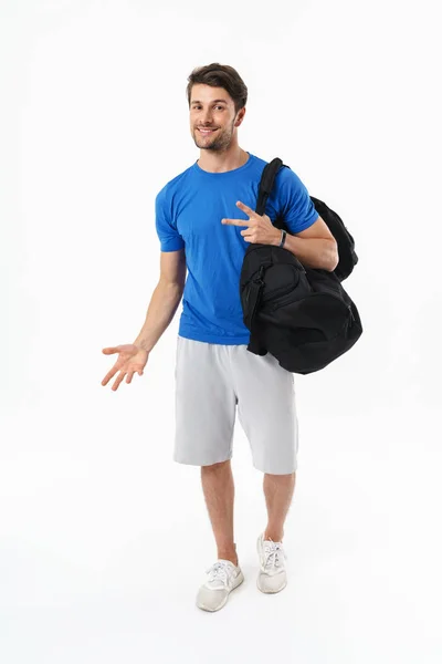 Allegro contento bello giovane sportivo fitness uomo in piedi isolato su parete bianca sfondo tenendo borsa fare gesto di pace . — Foto Stock