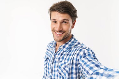 İyimser mutlu genç tıraşsız adam rahat gömlek giymiş beyaz duvar arka plan üzerinde izole poz kamera tarafından selfie çekmek.