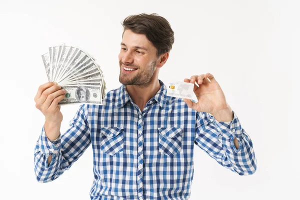 Feliz barbudo alegre sin afeitar hombre complacido vestido con camisa casual posando aislado sobre fondo blanco de la pared celebración de dinero y tarjeta de crédito . — Foto de Stock