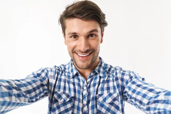 Gelukkig jong ongeschoren man gekleed in casual shirt poseren geïsoleerd over witte muur achtergrond Neem een selfie door camera. — Stockfoto