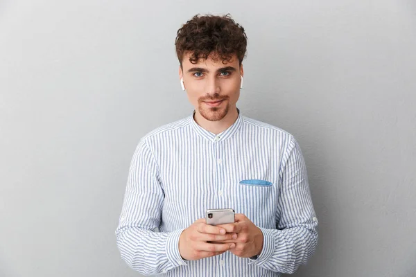 Image of caucasian young man with earpods looking at camera and holding cellphone — Stock Photo, Image