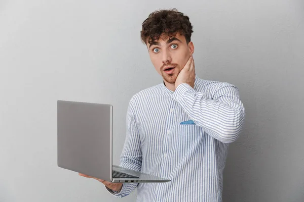 Πορτρέτο του προβληματισμένος Καυκάσιος άντρας ντυμένος σε πουκάμισο αναρωτώμενος ενώ κρατώντας και χρησιμοποιώντας ασημένιο φορητό υπολογιστή — Φωτογραφία Αρχείου