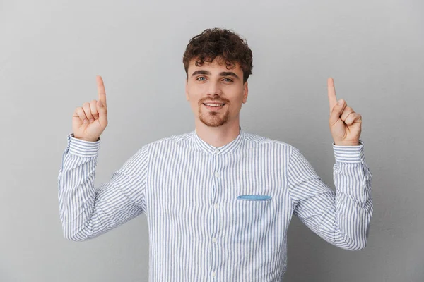 Portrait d'un bel homme caucasien vêtu d'une chemise souriant à la caméra et pointant les doigts vers le haut vers le copyspace — Photo