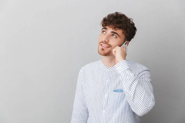 Retrato de morena hermoso hombre vestido con camisa sonriendo mientras sostiene y habla en el teléfono inteligente — Foto de Stock