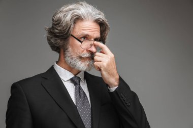 Resmi siyah takım elbise giyen ve kameraya bakan ve gözlüklerine dokunan konsantre yetişkin işadamının görüntüsü