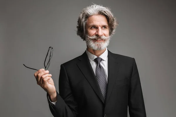 Bild eines fröhlichen erwachsenen Geschäftsmannes im formalen schwarzen Anzug, der in die Kamera lächelt und eine Brille hält — Stockfoto