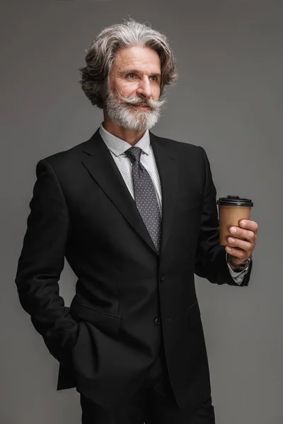 Bild eines erwachsenen kaukasischen Geschäftsmannes, der einen formalen schwarzen Anzug trägt, lächelt und Papierbecher in der Hand hält — Stockfoto