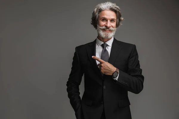 Bild eines gut aussehenden erwachsenen Geschäftsmannes, der einen formalen schwarzen Anzug trägt, lächelt und mit dem Finger auf Kopierraum zeigt — Stockfoto