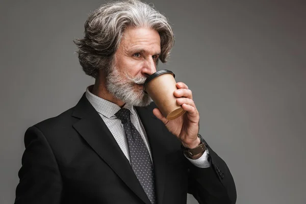 Bild eines bärtigen erwachsenen Geschäftsmannes im schwarzen Anzug, der Kaffee aus einer Papptasse trinkt — Stockfoto