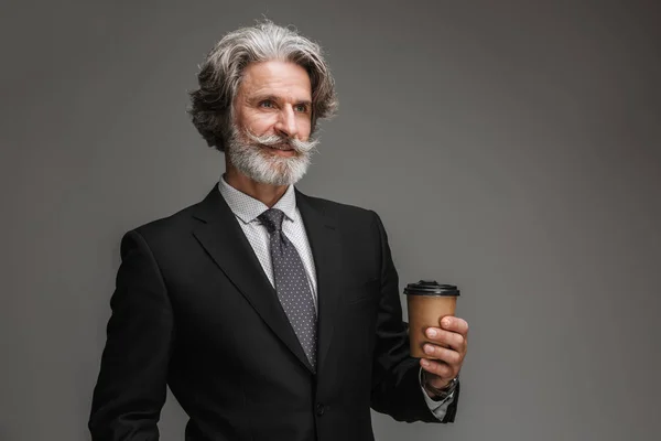 Bild eines unrasierten erwachsenen Geschäftsmannes, der einen formalen schwarzen Anzug trägt, lächelt und Pappbecher in der Hand hält — Stockfoto