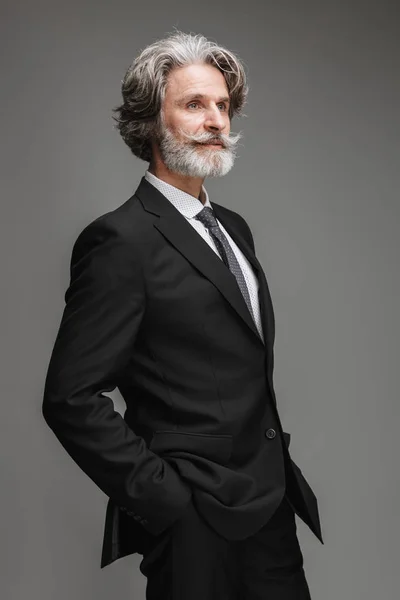 Bild eines selbstbewussten erwachsenen Geschäftsmannes im formalen schwarzen Anzug, der mit den Händen in den Taschen zur Seite schaut — Stockfoto