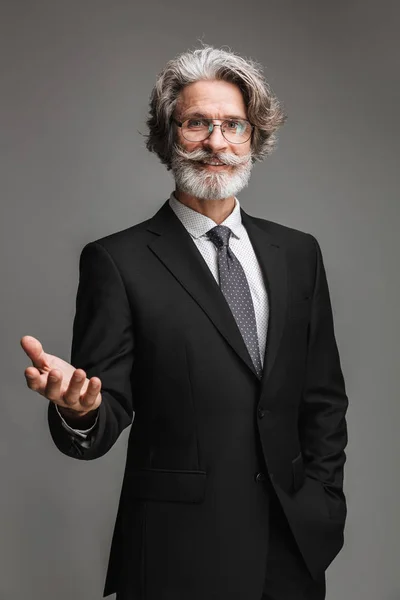 Bild eines fröhlichen erwachsenen Geschäftsmannes mit formalem schwarzen Anzug und Brille, der mit gestikulierender Hand in die Kamera lächelt — Stockfoto