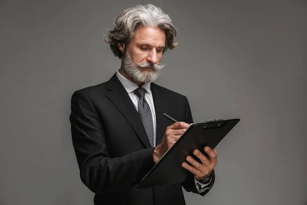 Image of caucasian adult businessman wearing formal black suit holding clipboard and writing down notes — Stock Photo, Image