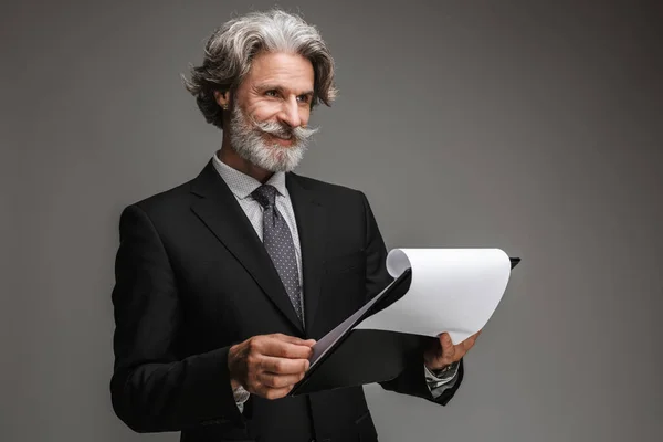 Bild eines erwachsenen Geschäftsmannes mit Schnurrbart, der einen formalen schwarzen Anzug trägt, lächelt und Papiertafeln in der Hand hält — Stockfoto