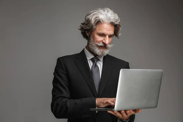 Bild eines gut aussehenden erwachsenen Geschäftsmannes im formalen schwarzen Anzug mit silbernem Laptop — Stockfoto