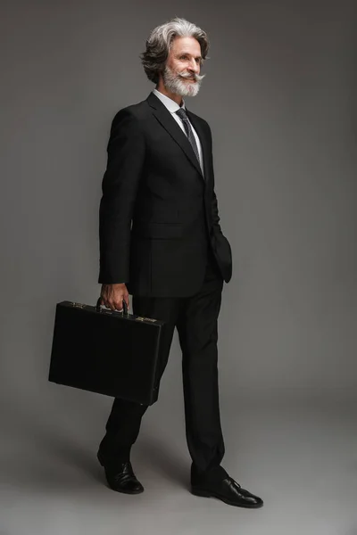 Bild in voller Länge von glücklichen erwachsenen Geschäftsmann trägt formalen schwarzen Anzug lächelnd und zu Fuß mit Aktentasche — Stockfoto