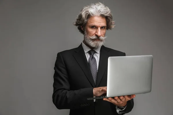 Image of serious adult businessman wearing formal black suit holding silver laptop — Stock Photo, Image