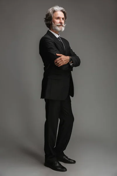 Ganzkörperbild eines unrasierten erwachsenen Geschäftsmannes im formalen schwarzen Anzug, der mit verschränkten Armen vor der Kamera steht — Stockfoto