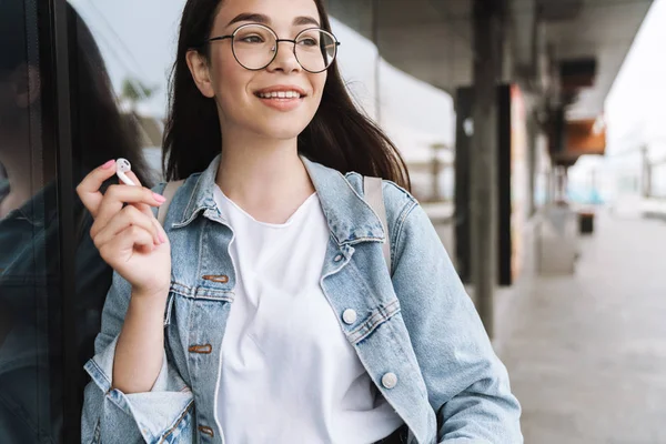 Feliz joven bonita estudiante con anteojos caminando al aire libre descansando escuchando música con auriculares . —  Fotos de Stock