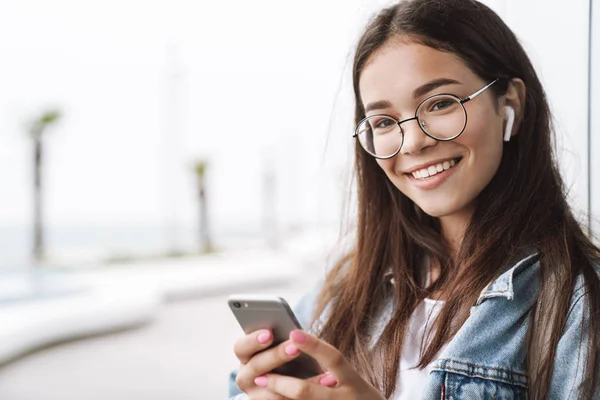 Bild av ganska leende tonårs flicka med hjälp av smartphone medan promenad — Stockfoto