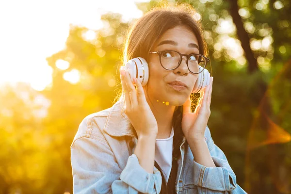 Gondolkodás fiatal tizenéves lány diák ül a szabadban, gyönyörű zöld parkban hallgat zenét fejhallgató. — Stock Fotó