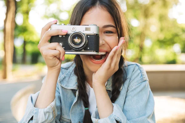 Mutlu sevimli genç öğrenci kız gözlük lüzumla doğa parkında bankta oturan kamera fotoğraflama tutarak. — Stok fotoğraf