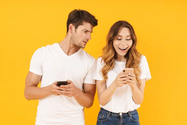 Fotografie mladého páru muže a ženy v základních tričkách, které drží a prohlížením mobilních telefonů — Stock fotografie