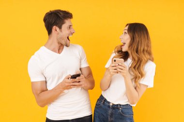 Akıllı telefonları tutarken birbirlerine bakan temel tişörtlü çekici çift erkek ve kadının portresi