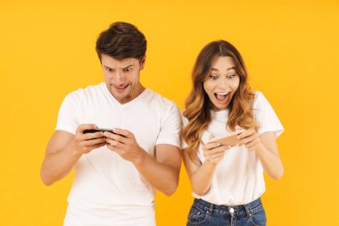 Akıllı telefonlarda video oyunları oynarken birlikte duran temel t-shirt neşeli çift erkek ve kadın Portresi