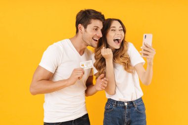 Kredi kartı ve akıllı telefon tutarken sevinen temel tişörtler içinde kafkas çiftin portresi