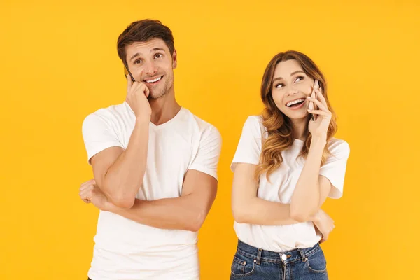 Porträt eines zufriedenen Paares in einfachen T-Shirts, das zusammen steht, während es auf Smartphones spricht — Stockfoto