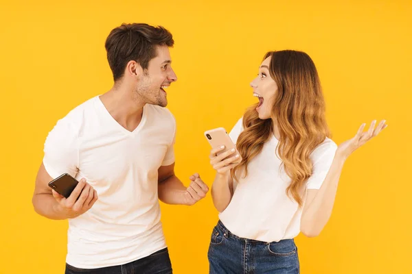 Porträtt av attraktiva par man och kvinna i grundläggande t-shirts tittar på varandra medan du håller smartphones — Stockfoto
