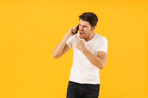 Homme hurlant mécontent en t-shirt blanc occasionnel parlant par téléphone mobile isolé sur fond jaune . — Photo