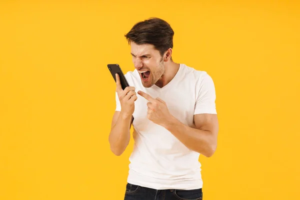 Homme hurlant mécontent en t-shirt blanc occasionnel parlant par téléphone mobile isolé sur fond jaune . — Photo